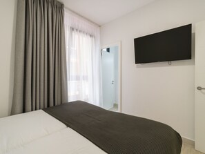 A hotel room with a bed, a television mounted on the wall, and a window with curtains.