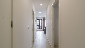 Un pasillo con paredes blancas y suelo de baldosas que lleva a una habitación con puerta corrediza de vidrio.