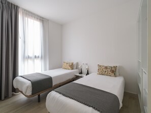 Una habitación de hotel con dos camas, una ventana con cortinas, lámparas de noche y un armario.