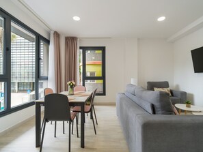 Una sala de estar moderna con un sofá gris, una mesa de comedor con sillas y un televisor montado en la pared.