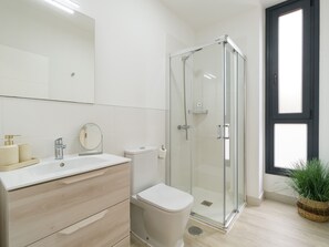 Un baño moderno con ducha de vidrio, lavamanos blanco y retrete.