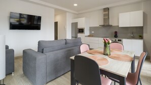 Una sala de estar moderna con un sofá gris, un televisor montado en la pared y un comedor con mesa y sillas de madera.
