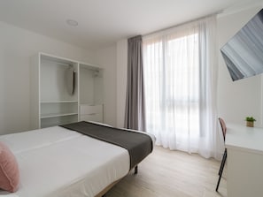 Quarto com cama, guarda-roupa, escrivaninha e janela com cortinas.