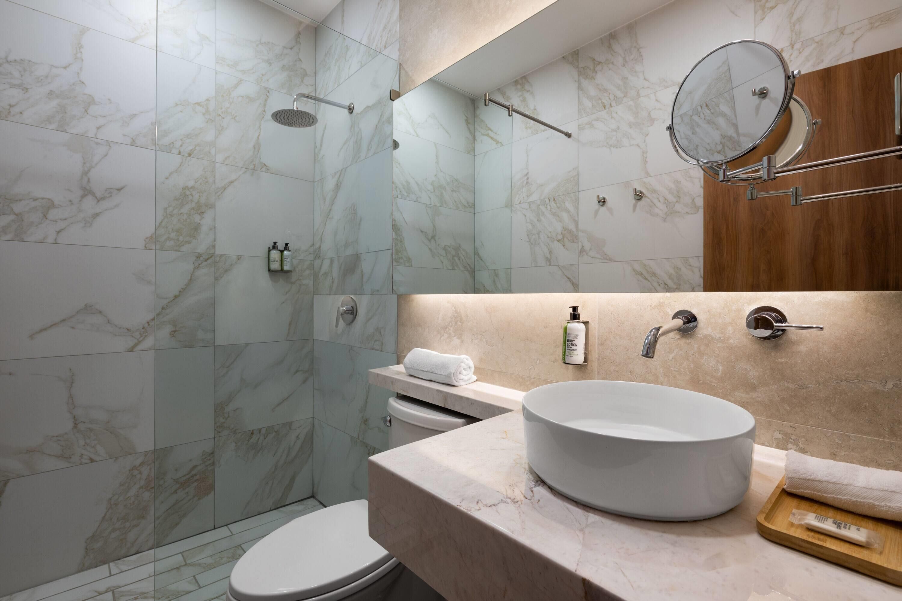 A modern bathroom with a marble shower, a toilet, a sink, and a mirror.