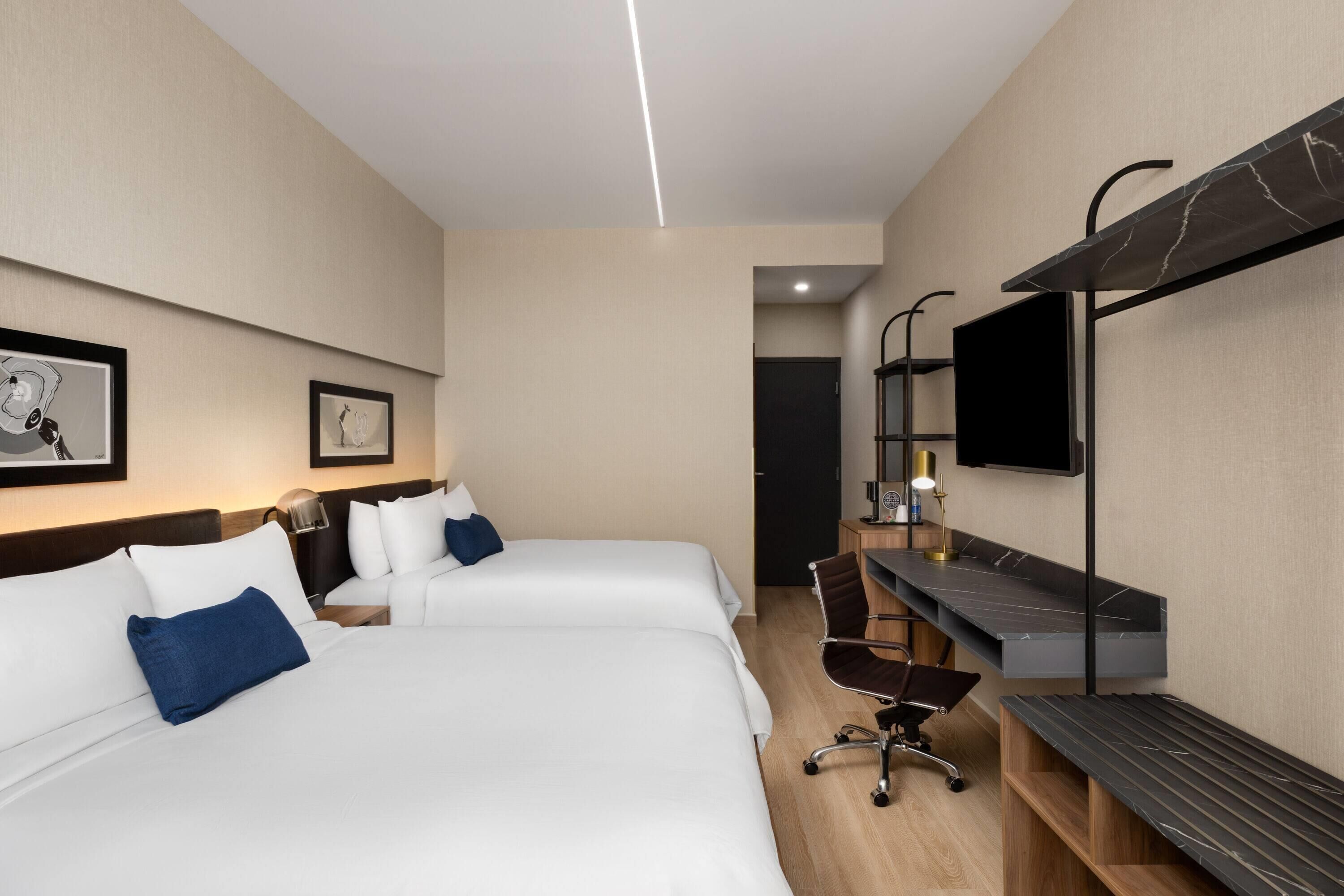 Een hotelkamer met twee bedden, een bureau, een stoel, een televisie en kunstwerken aan de muur.