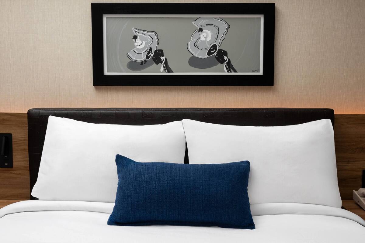 A neatly made bed with white and blue pillows, a framed artwork above it, and a wooden headboard.