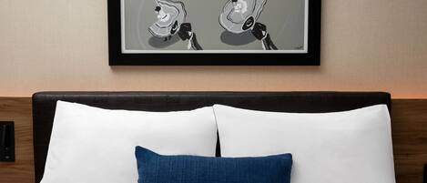 Una cama bien hecha con almohadas blancas y azules, una obra de arte enmarcada encima y un cabecero de madera.