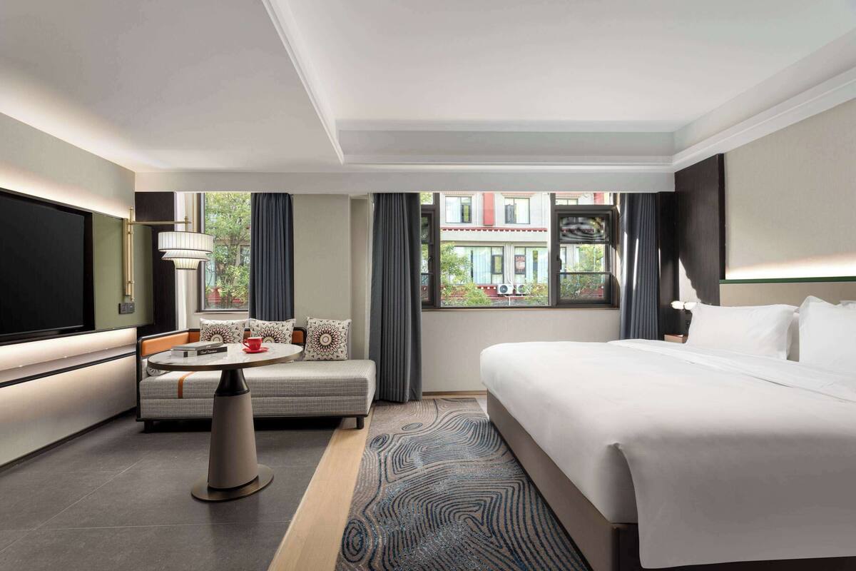A modern hotel room with a large bed, a sofa, a small table, and a TV.