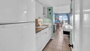 Una cocina moderna con armarios blancos, una encimera y un lavamanos. Se observa un comedor con una mesa y sillas al fondo.