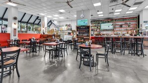 Un restaurante espacioso con numerosas mesas y sillas, una zona de bar y una cocina al fondo.