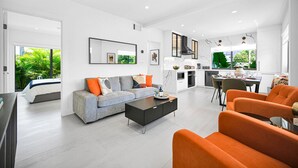 Una sala moderna con un sofá, una mesa de centro y sillas naranjas. Hay un comedor con una mesa y sillas, y una cocina con estufa y armarios.