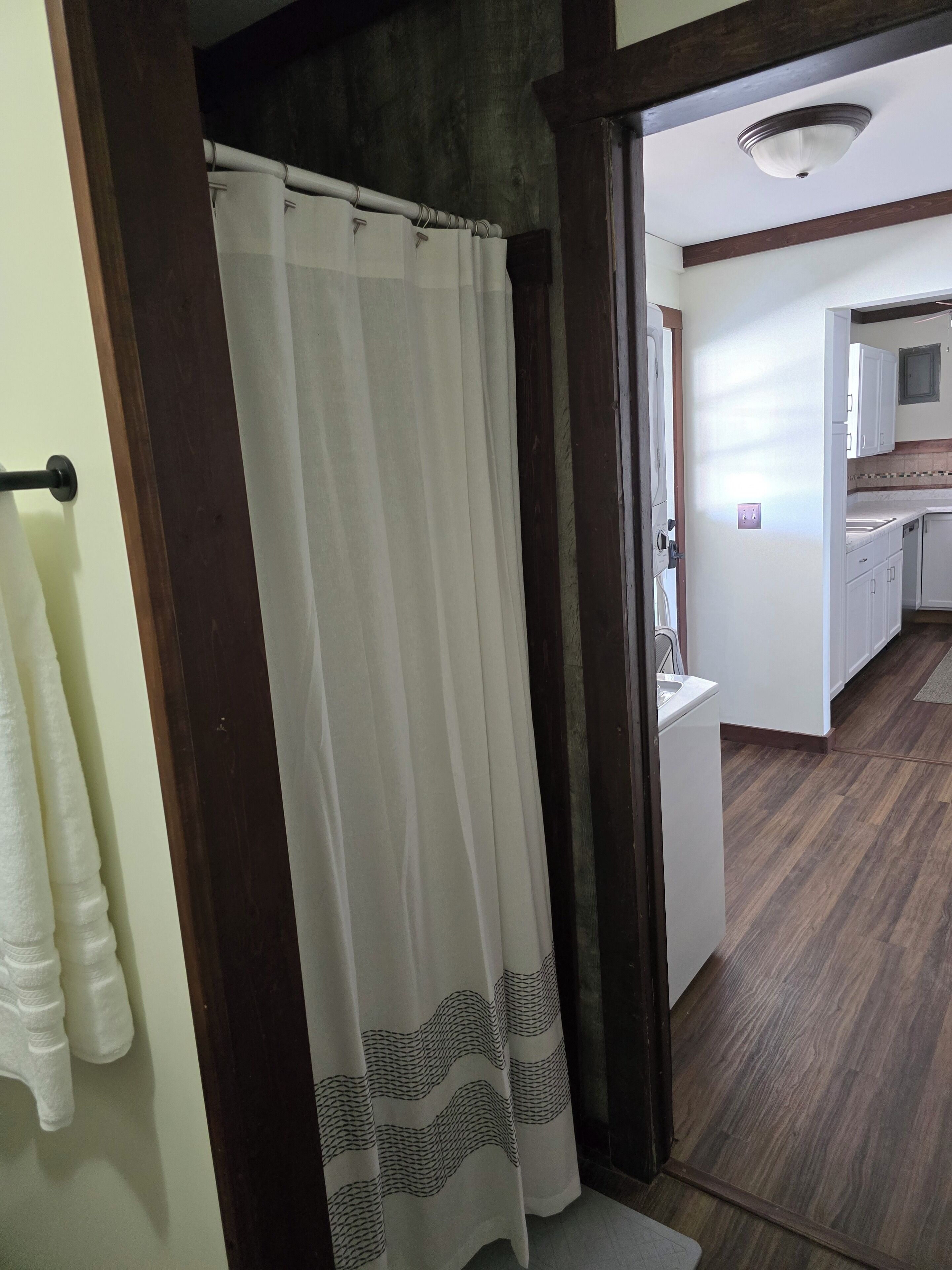 A bathroom with a shower curtain, a towel rack, and a wooden floor.