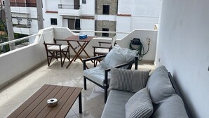 En balkong med ett träbord, en grå soffa med randiga kuddar och ett hopfällbart bord med stolar.