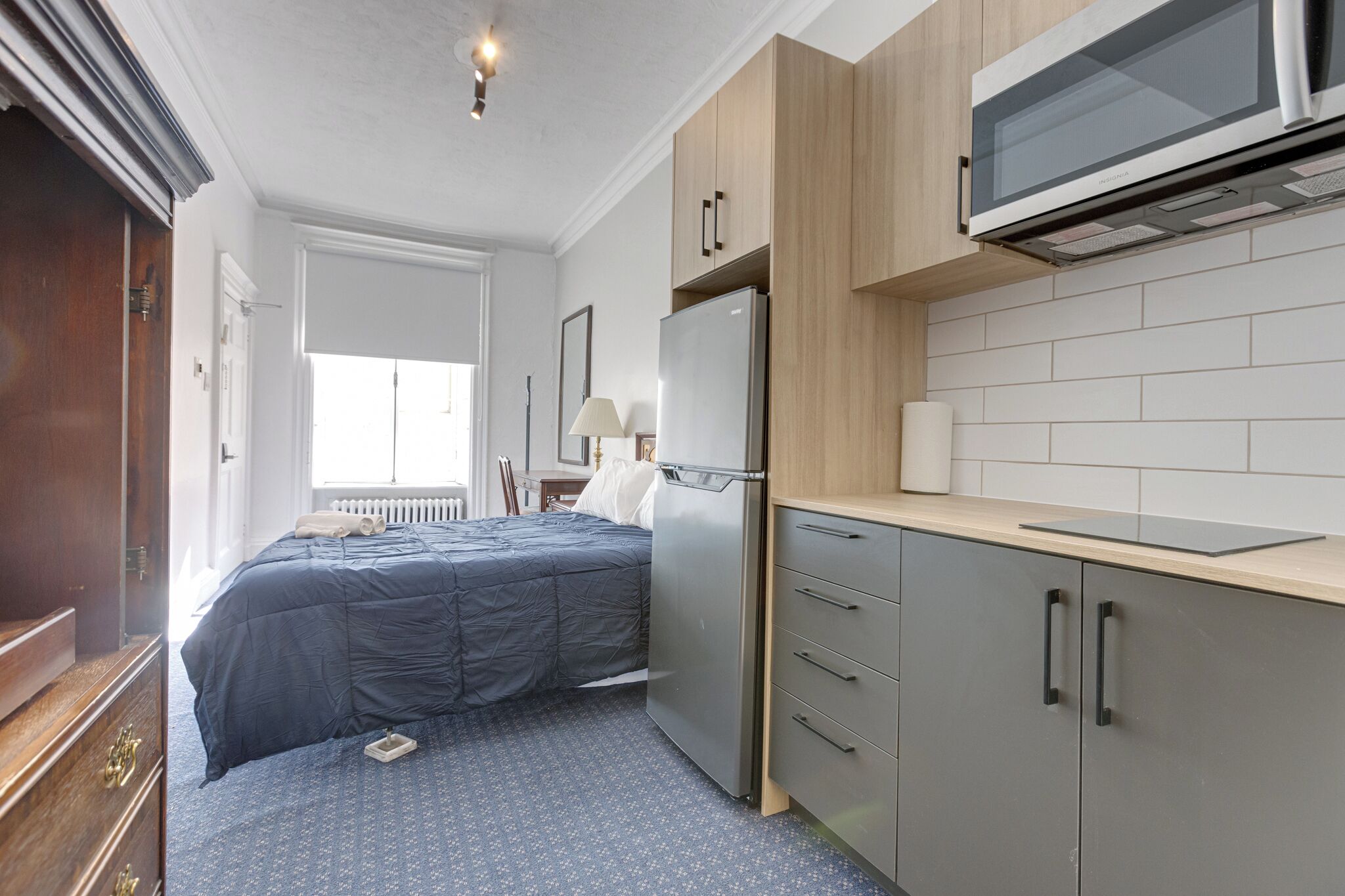 Une chambre d’hôtel de taille réduite, équipée d’un lit, d’un réfrigérateur, d’un four à micro-ondes et d’une petite kitchenette.