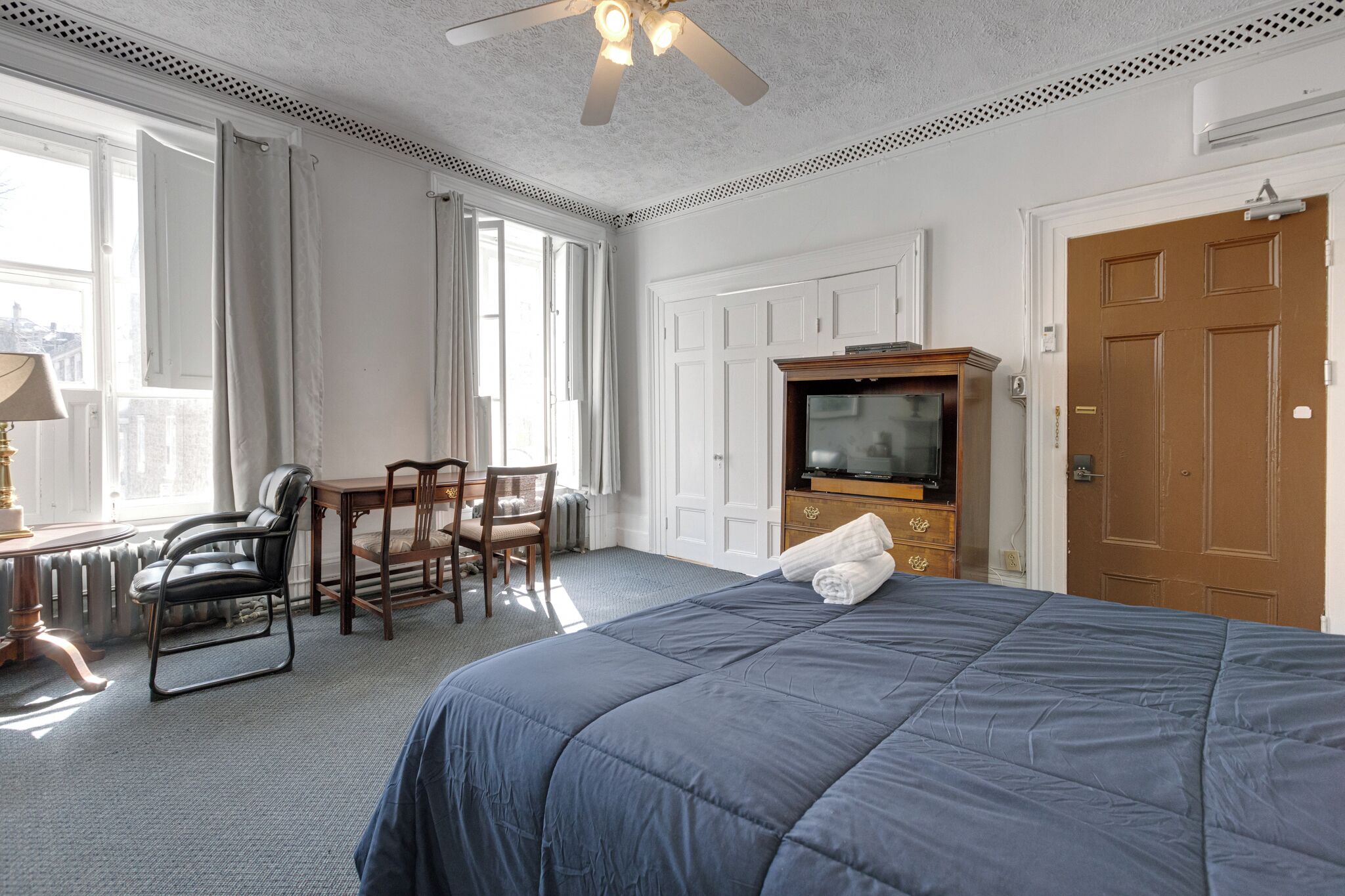 Habitación de hotel con una cama grande, un escritorio con silla, un televisor y un armario.