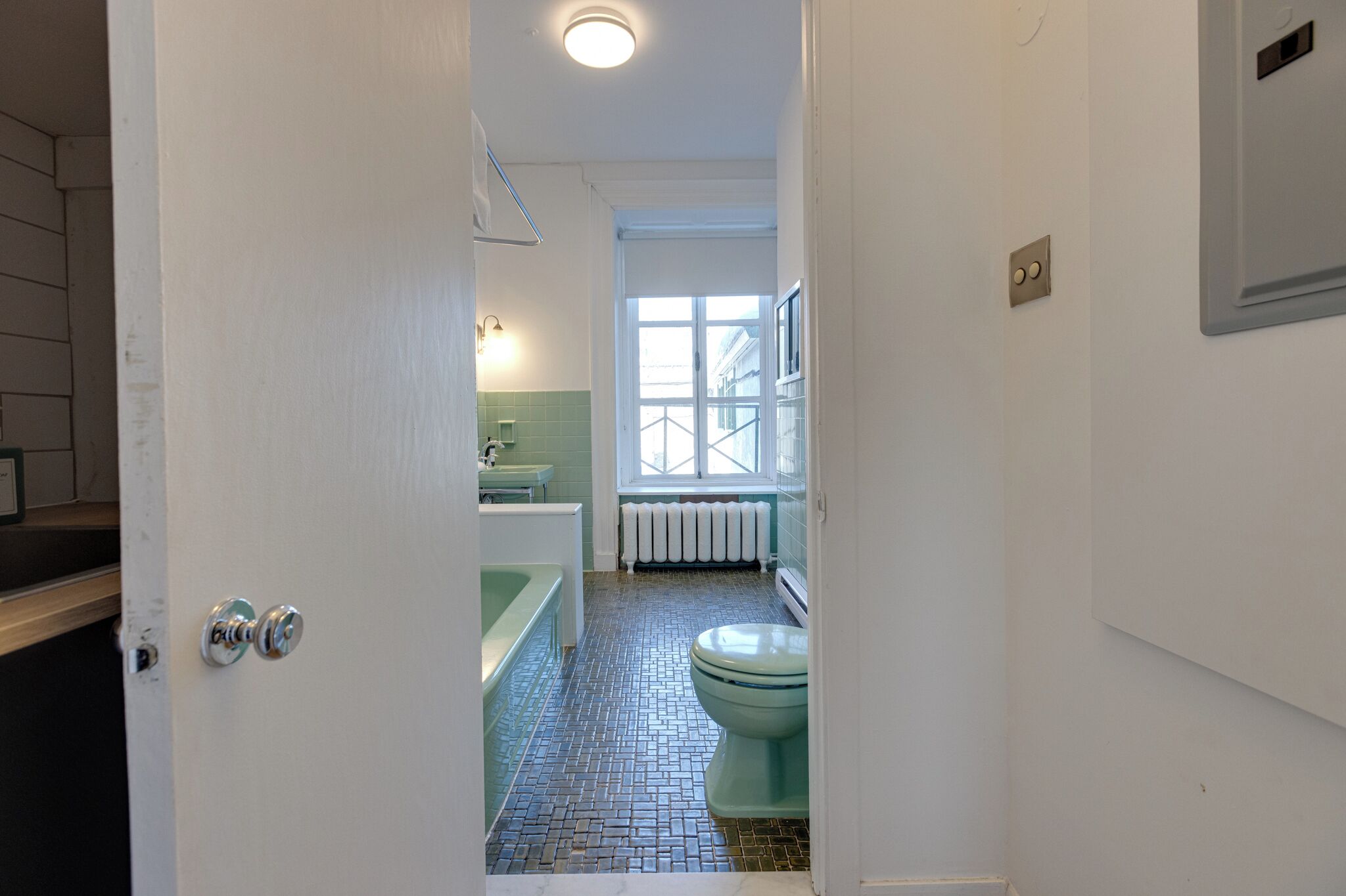 Un baño estrecho con suelo de baldosas, inodoro, bañera y ventana que proporciona luz natural.