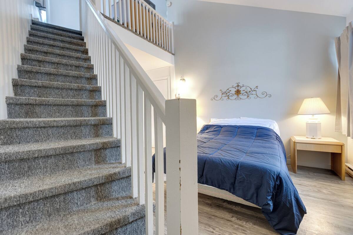 A bedroom with a bed, a nightstand, a lamp, and a staircase.