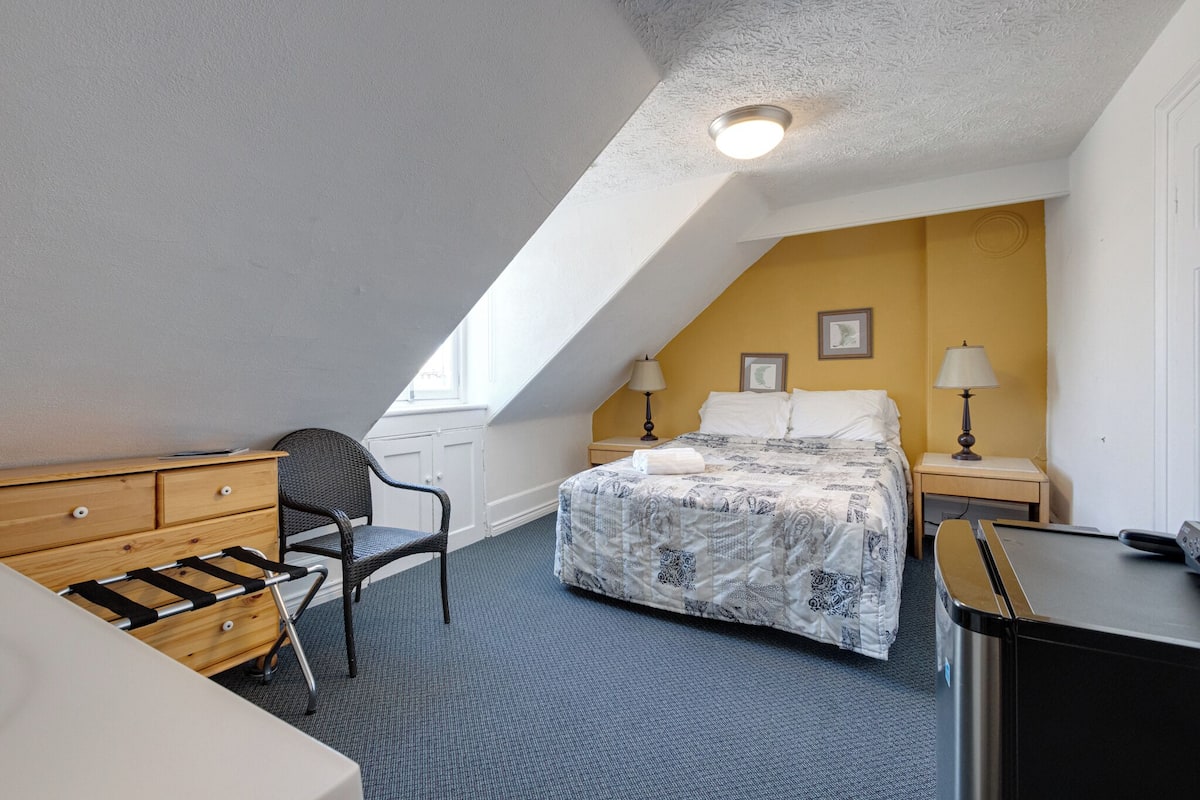 A bedroom with a bed, a dresser, a chair, a desk, and a washing machine.