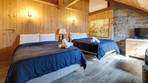 Een houten kamer met twee bedden, een stenen muur, een schilderij en een televisie.