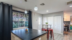 A modern kitchen with a black countertop, a window with a view of greenery, and a small dining area with a table and chairs. - Minutes to Old Town & Stadium, Hot Tub, Fire Pit, Pool, Bar, Gazebo, Sleeps 14 (Scottsdale)