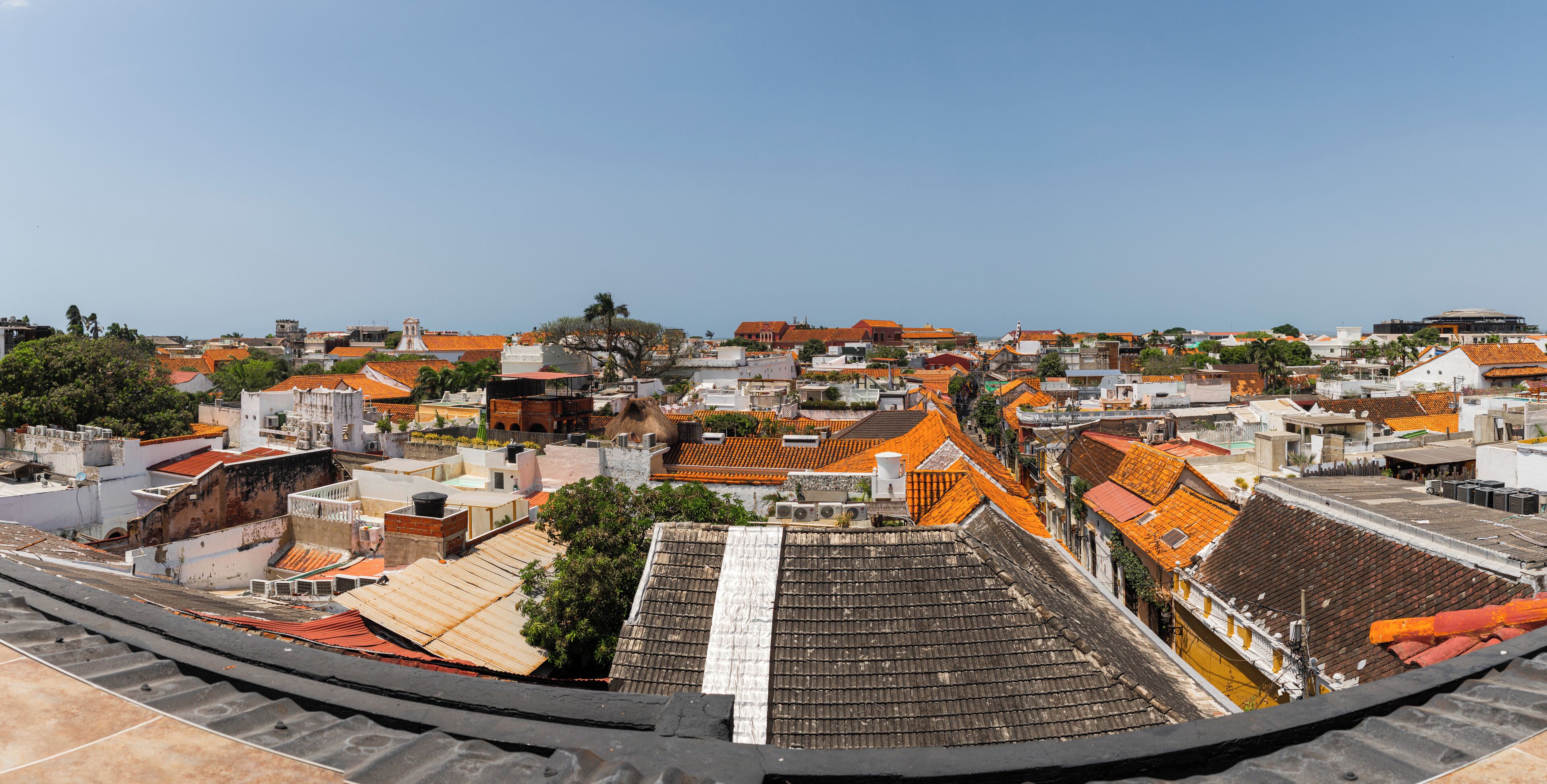 Vista panorámica de un pueblo costero con diversos edificios, incluyendo viviendas y locales comerciales, y una iglesia destacada con un campanario.