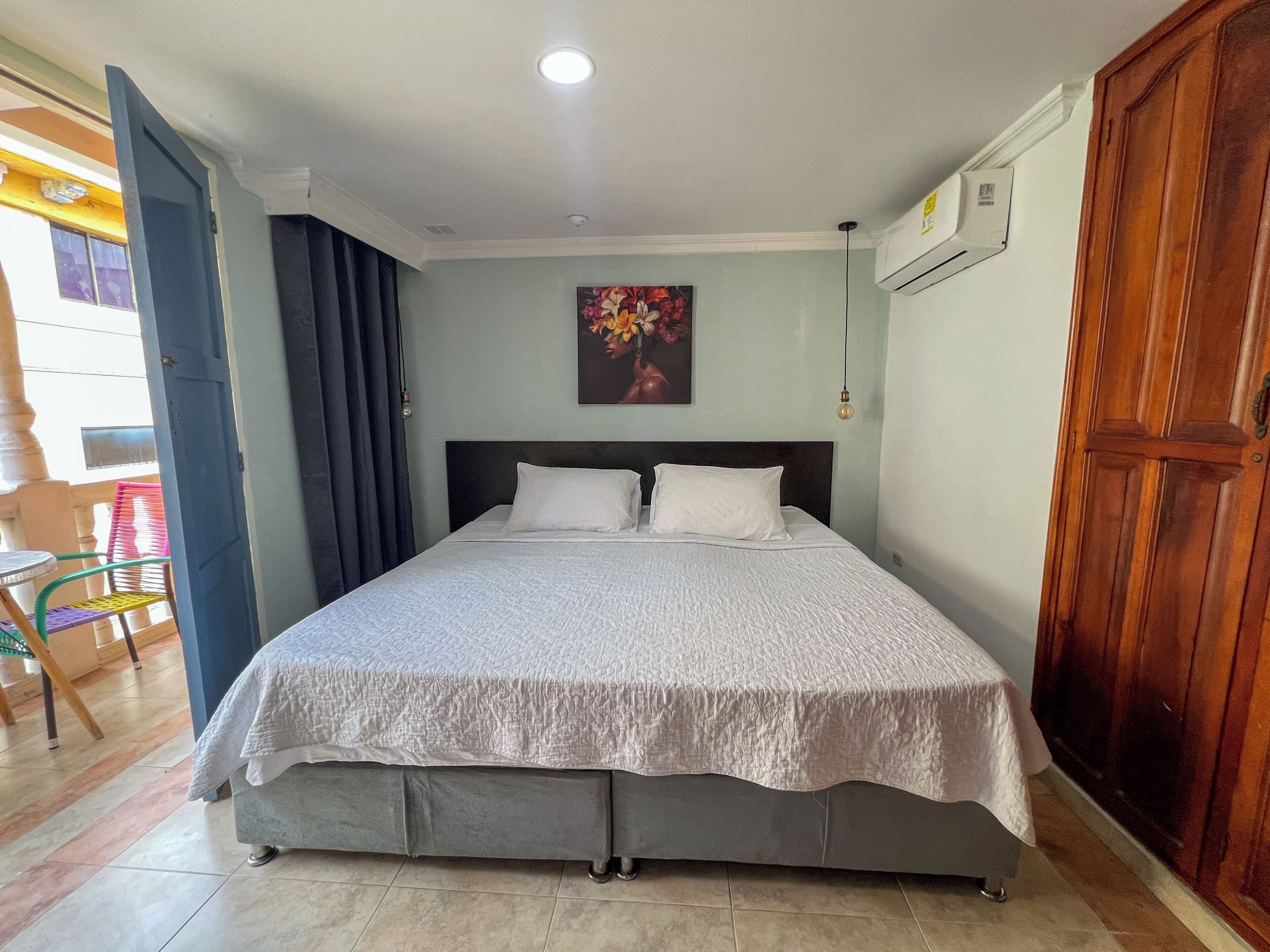 A bedroom with a bed, a painting on the wall, and a wooden door.