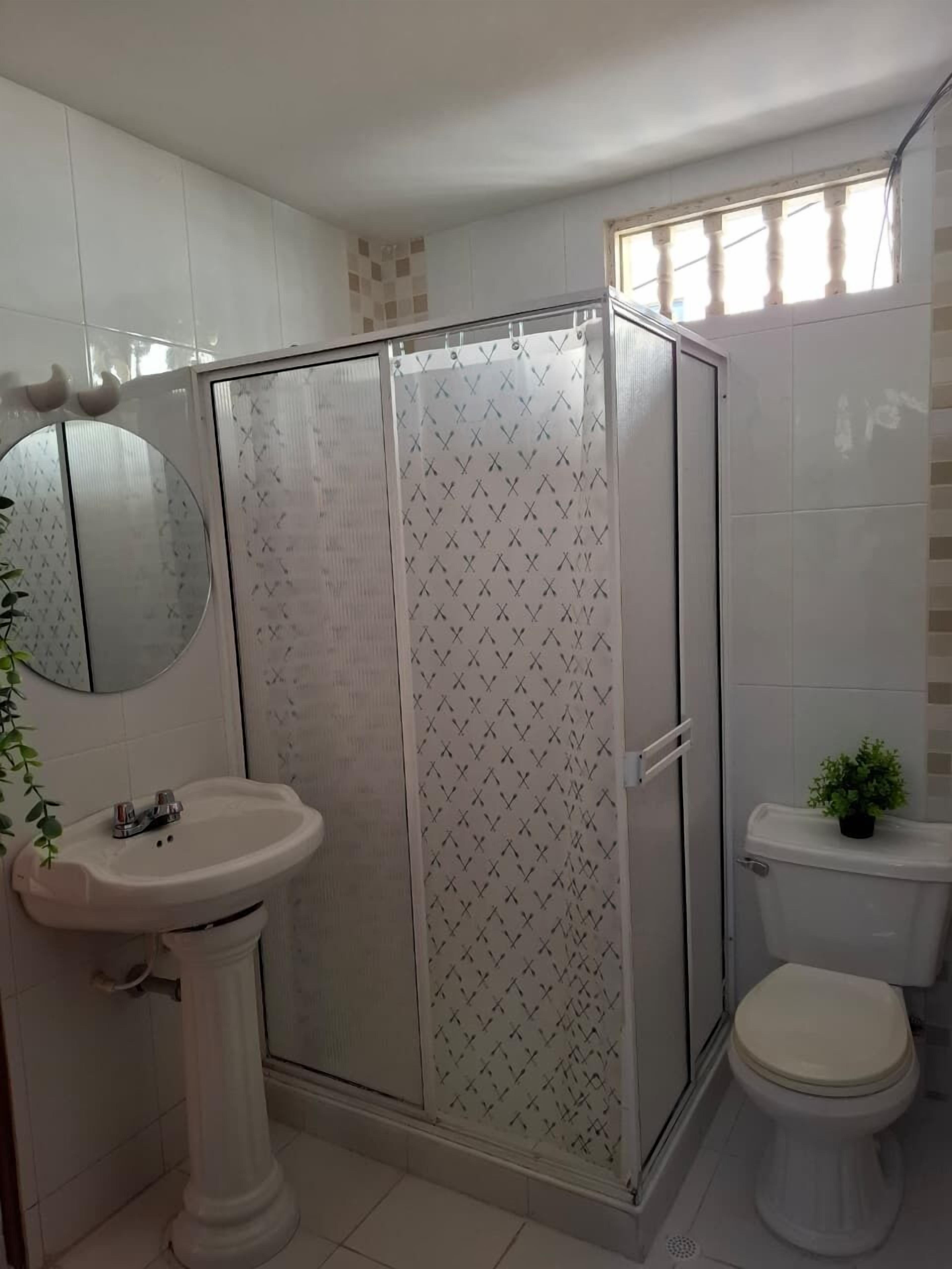 Un baño con ducha de vidrio, lavamanos pedestal, inodoro y espejo.