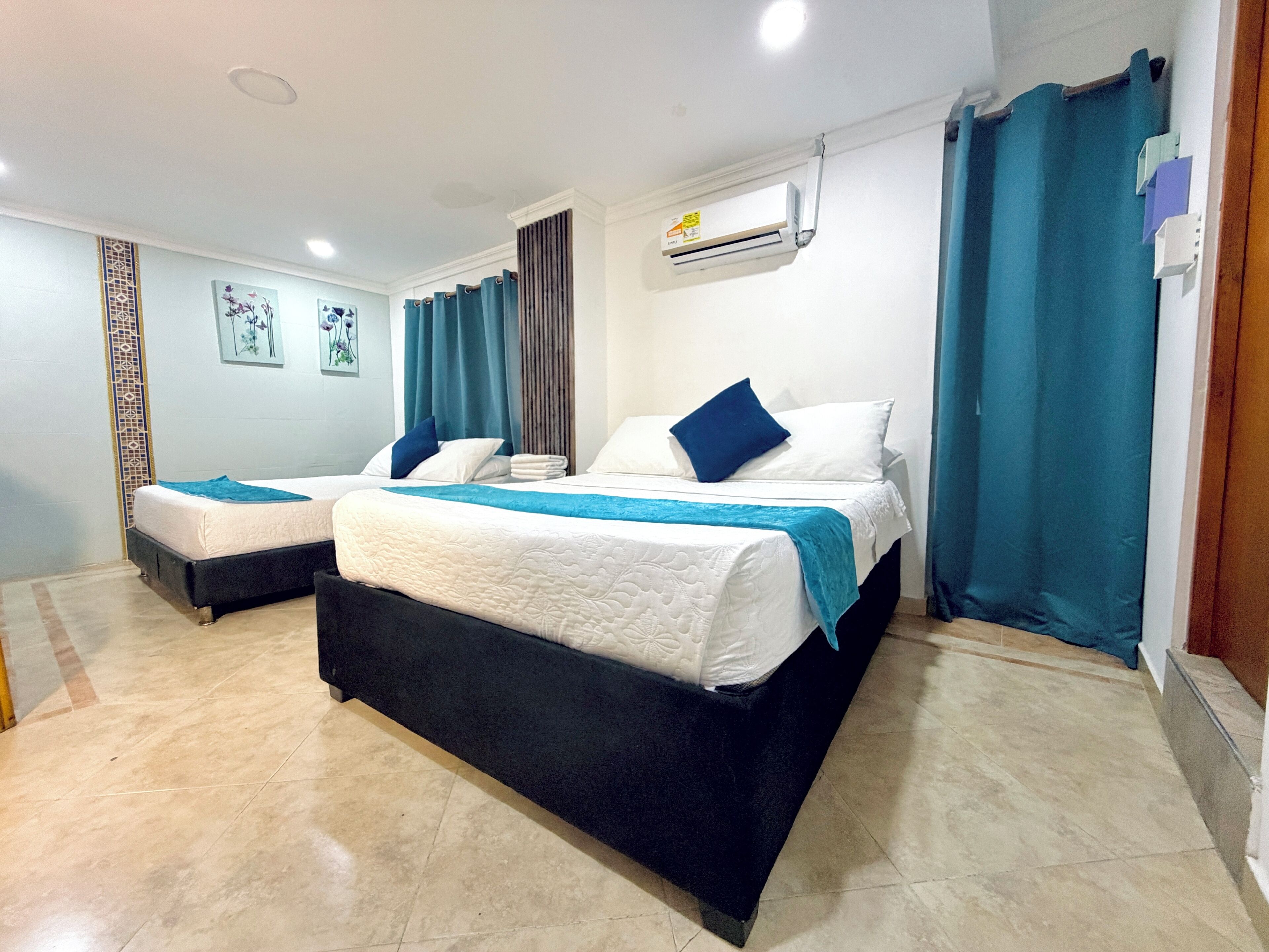 A hotel room with two beds, a ceiling fan, an air conditioning unit, and a window with curtains.