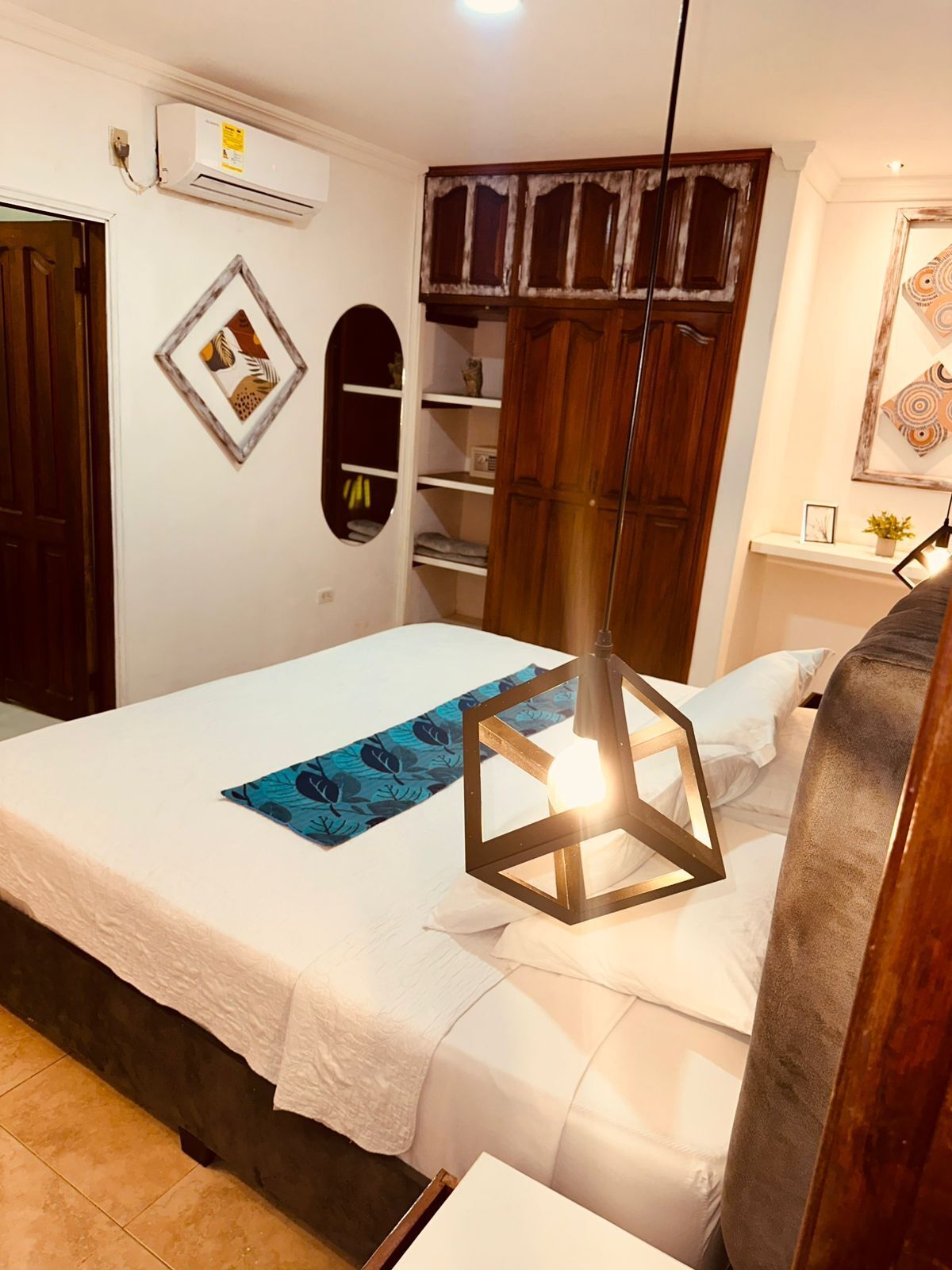 Une chambre à coucher comprenant un lit, une armoire, une étagère avec des objets décoratifs et un climatiseur fixé au mur.