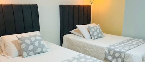 A hotel room with two beds, each with a headboard and pillows. There are wall art pieces above the beds and a pendant light hanging above.