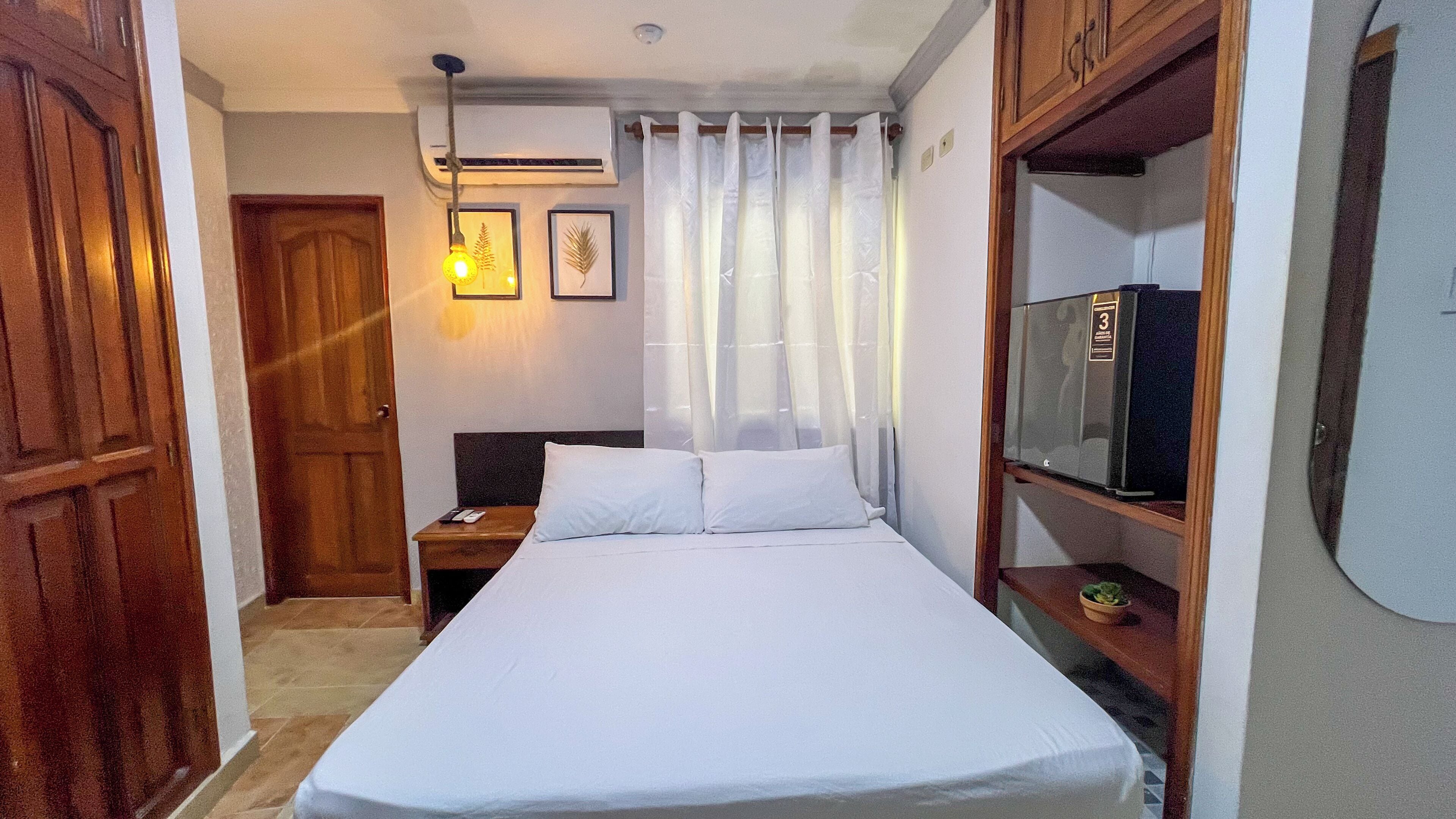 A hotel room with a bed, a nightstand, a TV, and a wooden wardrobe.