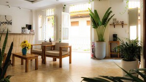 Un salón amplio con un sofá de madera, una mesa de centro y una planta en maceta. Una ventana grande permite que entre luz natural en la habitación.
