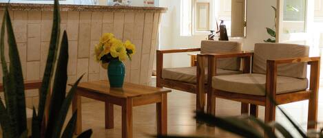 A reception area with a counter, wooden chairs, a vase of yellow flowers, and a potted plant.