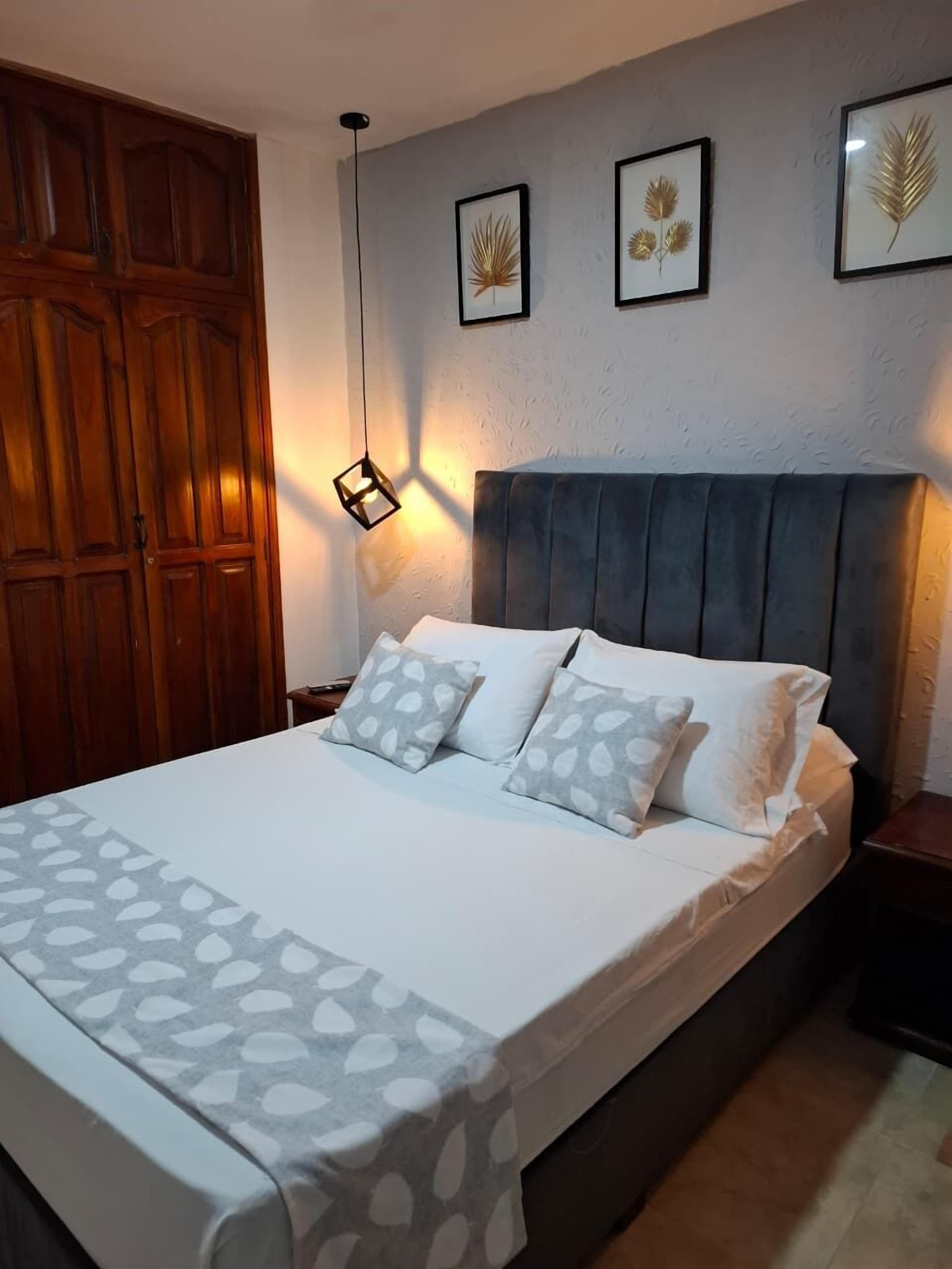 Ein Schlafzimmer mit einem Bett, einem Nachttisch, einem Holzschrank und drei gerahmten Wandbildern.