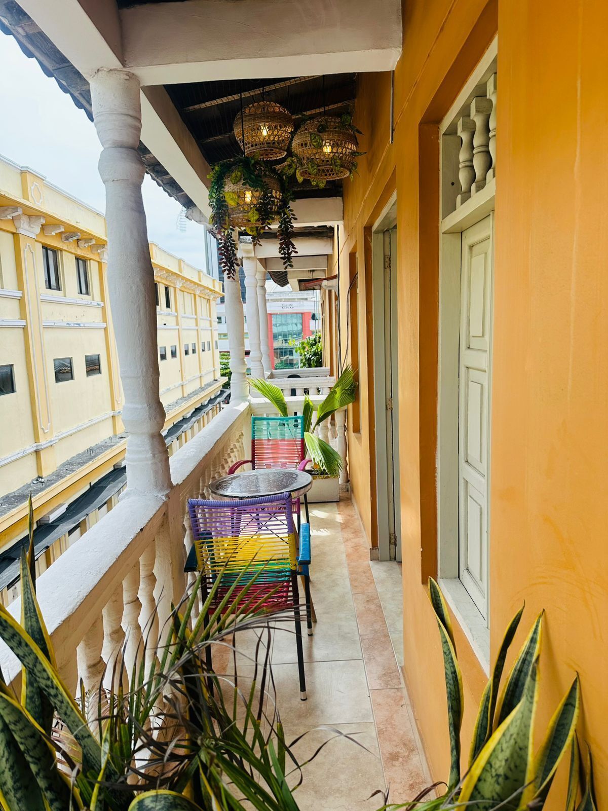 Een balkon met kleurrijke stoelen en planten in potten, met uitzicht op een stadsgezicht.