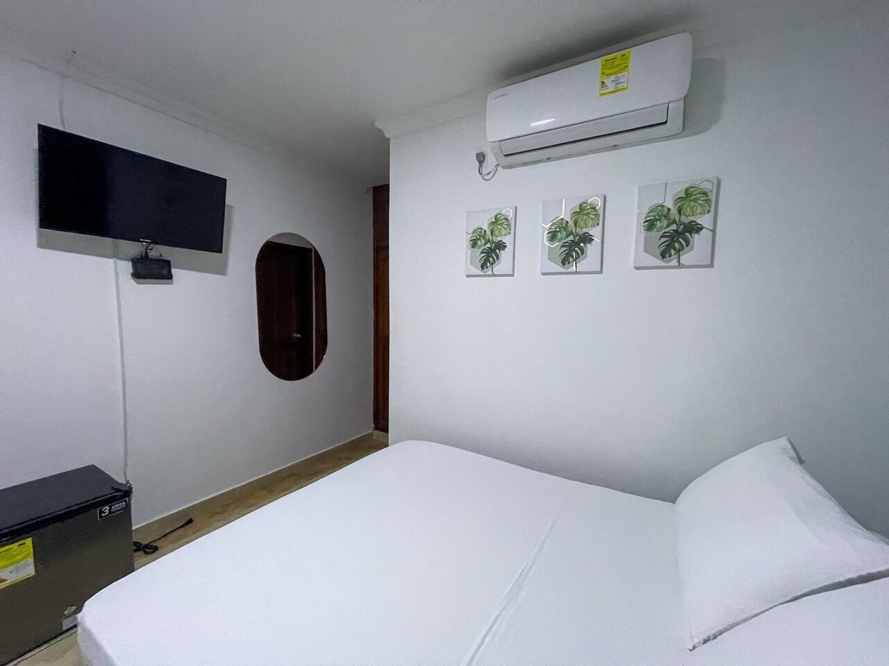 A room with a bed, a TV, an air conditioner, and wall art.