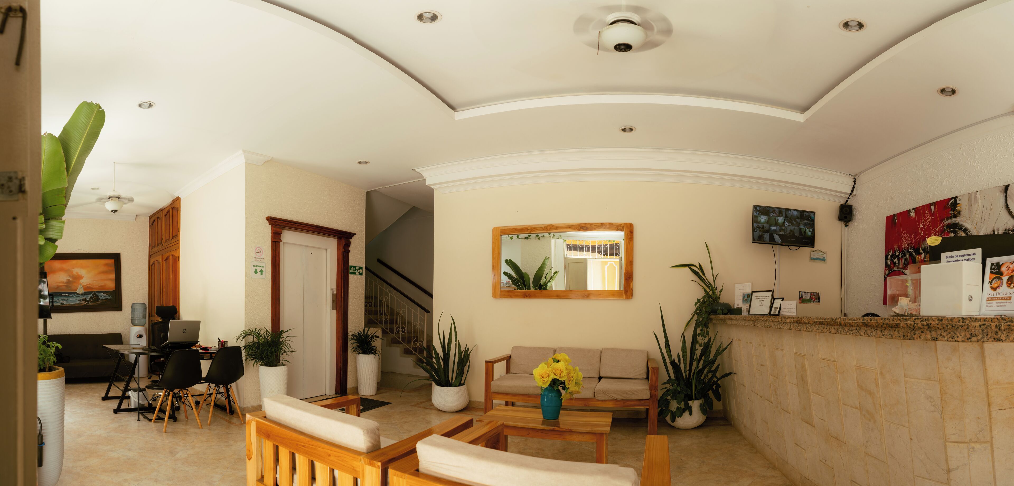 A hotel lobby with a reception desk, seating area, staircase, and a large mirror.