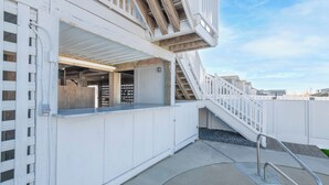 Un espace piscine doté d’une terrasse blanche, d’une échelle en métal et d’un escalier menant à une terrasse couverte.