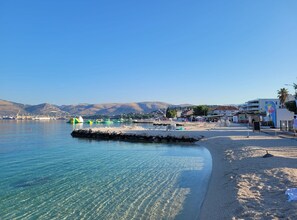 A beach with clear water, a pier, and buildings in the background.