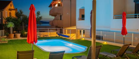 A swimming pool with lounge chairs and umbrellas, surrounded by a well-maintained lawn and a building with balconies.