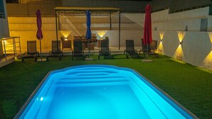 Une piscine intérieure dotée d’un élément décoratif aquatique illuminé de lumière bleue, entourée de chaises longues et de parasols.