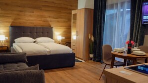 A modern hotel room with a wooden headboard bed, a sitting area with a sofa and a dining table set for two, and a TV mounted on the wall. - Apartments Neli - Studio Standard (Okrug Gornji)