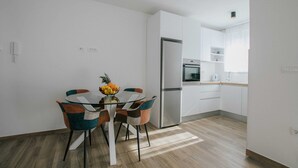 Eine moderne Küche mit weißen Schränken, einem Edelstahl-Kühlschrank und einem Essbereich mit einem Glastisch und bunten Stühlen.