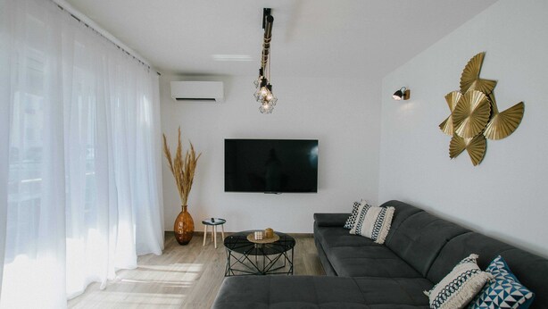 Ein modernes Wohnzimmer mit einem dunkelgrauen Sofa, einem Flachbildfernseher, einer Wanddekoration und einer Pendelleuchte.