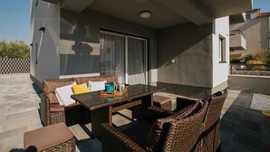 Ein Terrassenbereich im Freien mit Korbmöbeln, einem Tisch mit Glasplatte und einer Glastür.