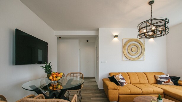 A modern living room with a glass dining table, wicker chairs, a mustard-colored sofa, and a unique ceiling light fixture. - Spacious Luxury Trogir Apartments - Comfort Two Bedroom Apartment (Trogir)