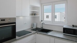 A modern kitchen with white cabinetry, a built-in oven, a microwave, and a window with a view of buildings. - Spacious Luxury Trogir Apartments - Standard Two Bedroom Apartment (Trogir)