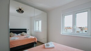 A bedroom with a bed, a large mirror, a window, and a view of buildings outside. - Spacious Luxury Trogir Apartments - Standard Two Bedroom Apartment (Trogir)