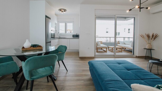 A modern living room with a blue sofa, teal chairs, and a glass dining table. - Spacious Luxury Trogir Apartments - Standard Two Bedroom Apartment (Trogir)