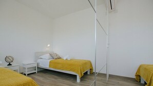 A modern, minimalist bedroom with a large mirror, two beds with yellow bedding, white headboards, and a small bedside table with a lamp. - Spacious Luxury Trogir Apartments - Superior Two Bedroom Apartment (Trogir)